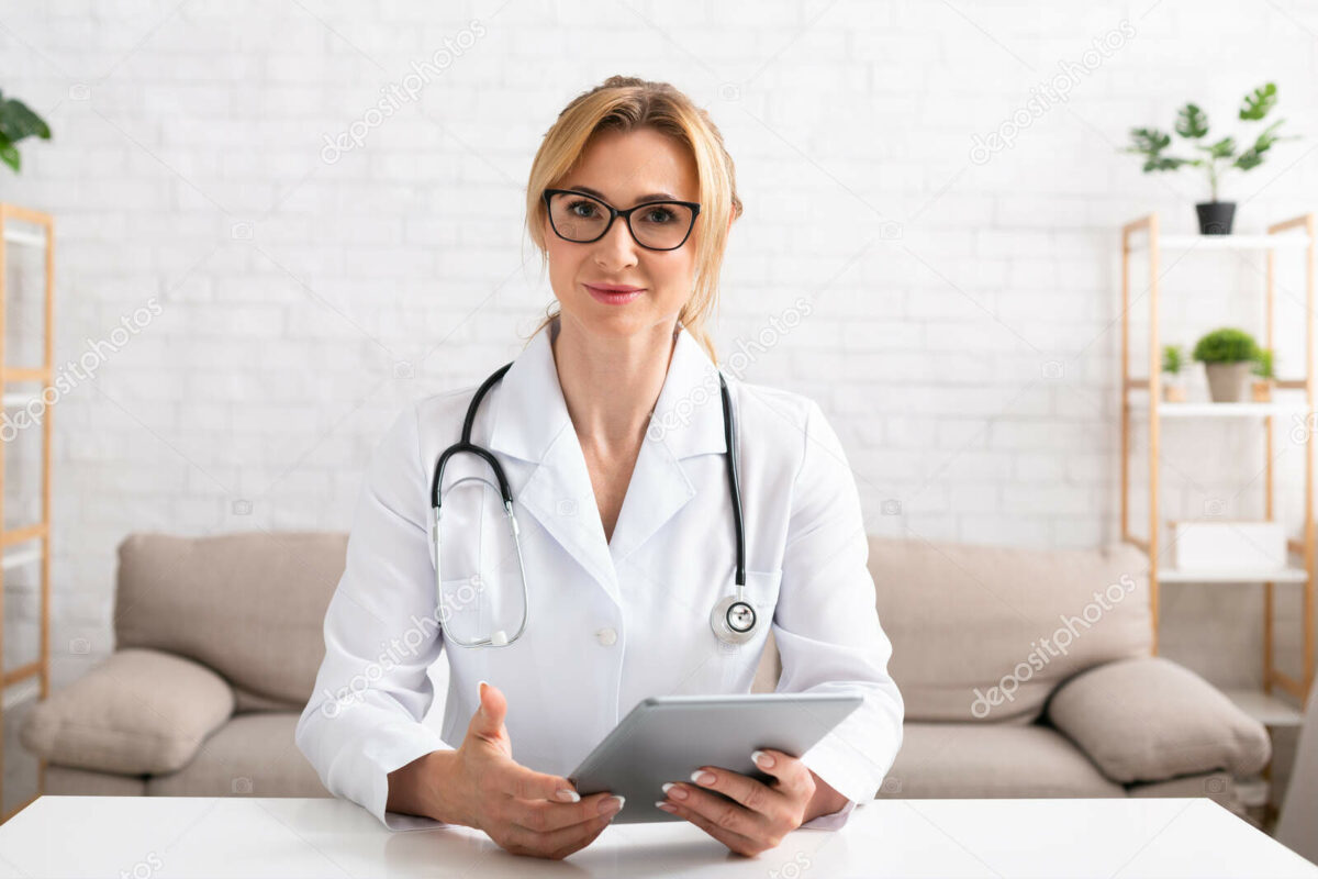 Contact with patients online. Woman doctor with glasses and white coat holds digital tablet in hands